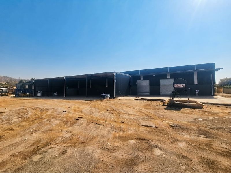Industrial warehouse facility featuring metal cladding, roller shutter doors, a covered loading area, and an expansive unpaved yard space.