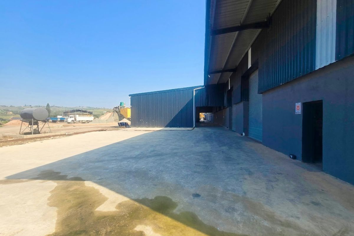 Industrial exterior view featuring a large concrete yard, corrugated metal warehouse cladding, and multiple roller shutter access doors.