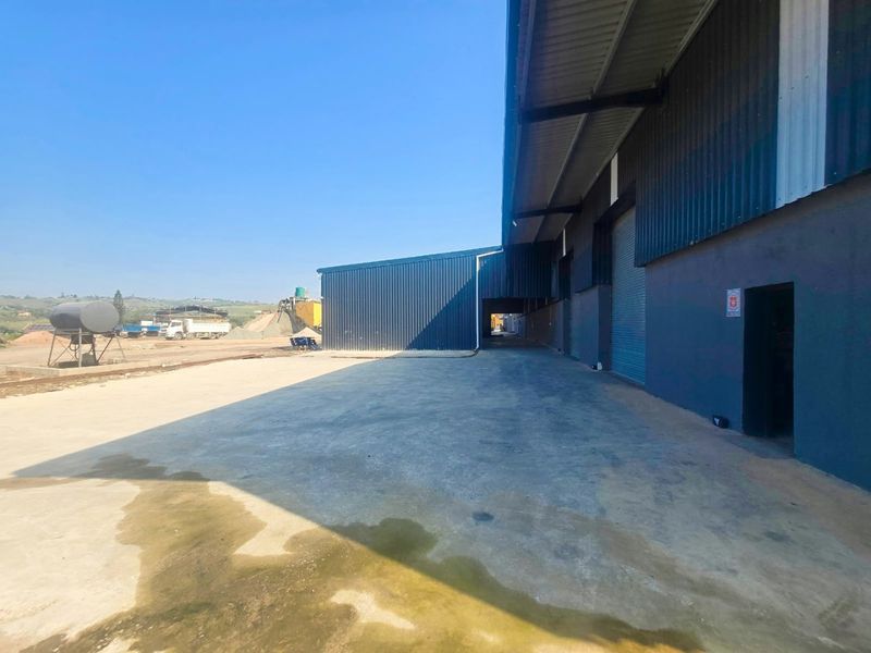 Industrial exterior view featuring a large concrete yard, corrugated metal warehouse cladding, and multiple roller shutter access doors.