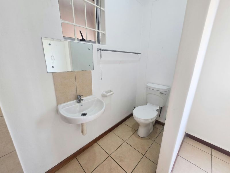 A compact bathroom featuring a wall-mounted basin, toilet, and tiled flooring, requiring minor cosmetic updates to improve its overall appearance.