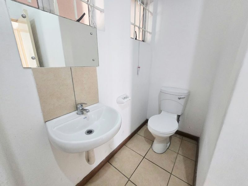 A compact bathroom featuring a wall-mounted basin, toilet, tiled flooring, and a wall mirror, providing essential functionality in a simple, clean layout.