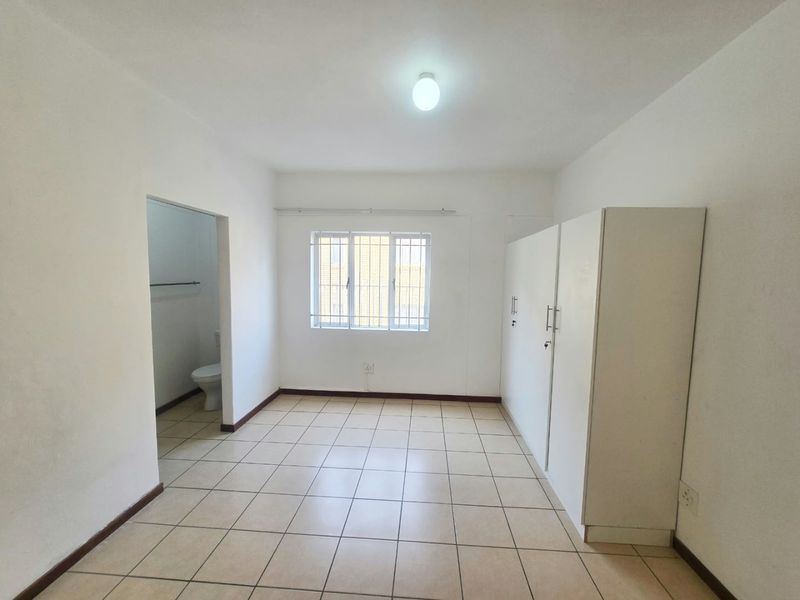 A bright, empty bedroom featuring tiled flooring, built-in cupboards, and an en-suite bathroom access point.