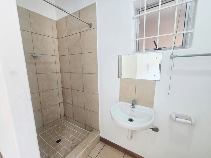 A functional bathroom featuring a tiled shower enclosure and a wall-mounted basin, requiring some cosmetic updates to improve its overall condition.