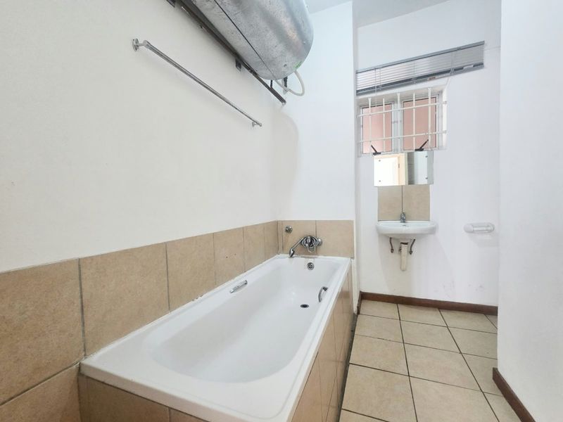 A functional bathroom featuring a bathtub, wall-mounted basin, and tiled finishes, currently awaiting modernization to improve its aesthetic appeal.