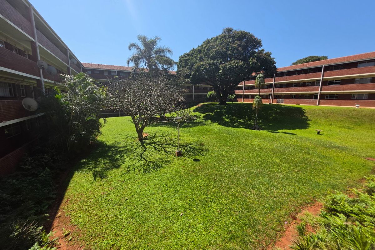 A view of the communal garden area surrounded by the brick apartment building complex, featuring mature trees and well-maintained lawn space.
