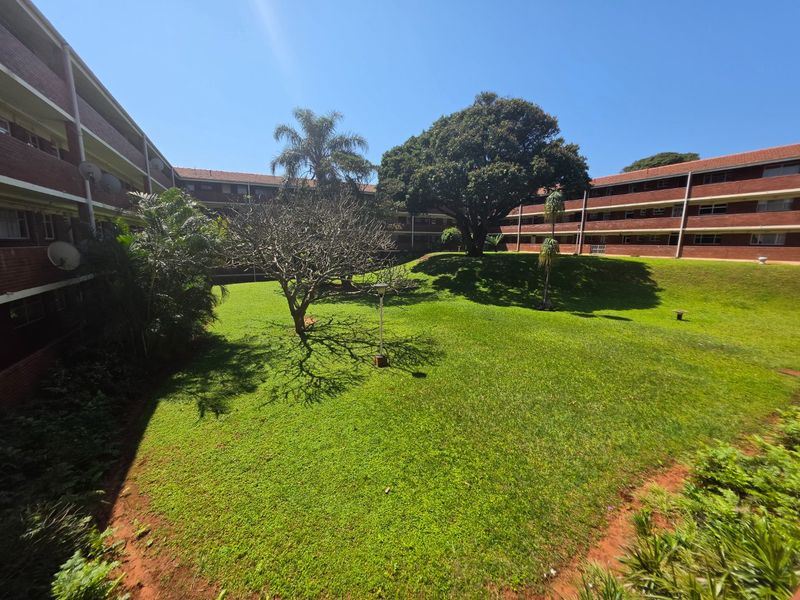 A view of the communal garden area surrounded by the brick apartment building complex, featuring mature trees and well-maintained lawn space.