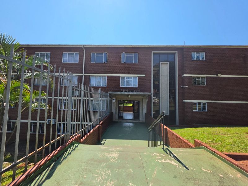 Front elevation of the Pencelly apartment building featuring a brick facade, secure gated entrance, and a concrete walkway leading to the main building access.
