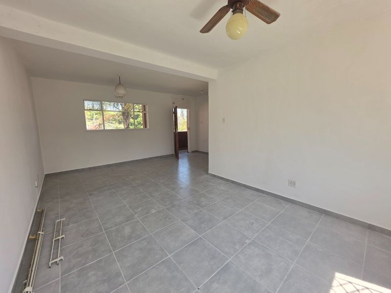 An empty, open-plan living area featuring neutral grey tiled flooring, a ceiling fan, and natural light from the window.