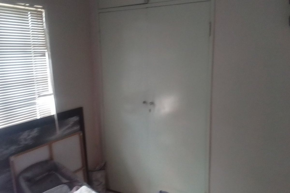 A bedroom featuring a built-in wardrobe and a window fitted with venetian blinds.