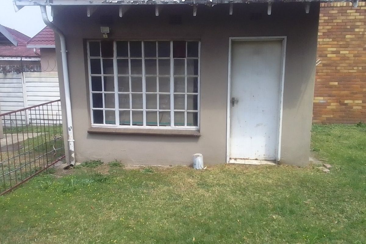 Rear exterior view of the property showing a small structure with a grid-pattern window and a single access door.