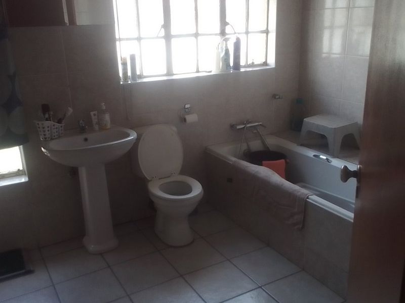 A functional bathroom featuring a pedestal basin, toilet, and built-in bathtub with tiled walls and flooring.