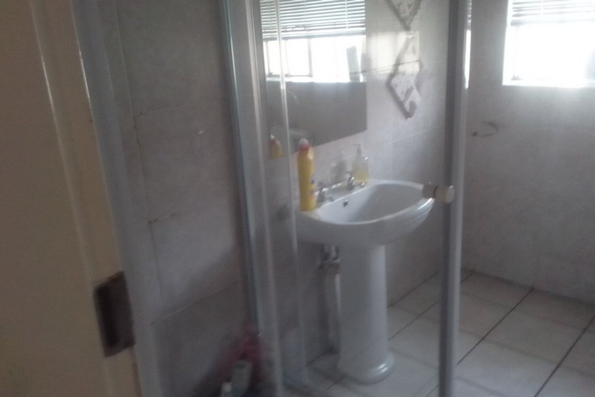 A functional bathroom featuring a pedestal basin, tiled walls and flooring, and a glass-enclosed shower area.