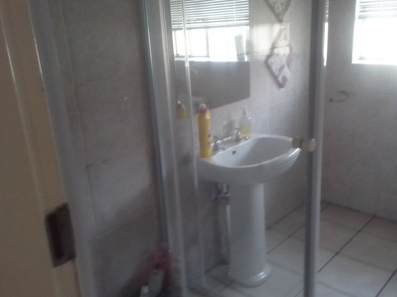 A functional bathroom featuring a pedestal basin, tiled walls and flooring, and a glass-enclosed shower area.