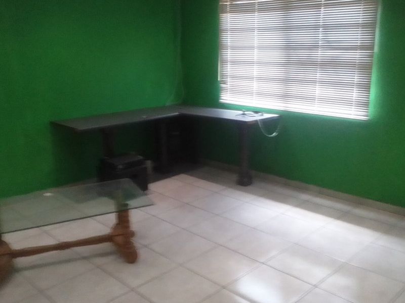 A simple office space featuring tiled flooring, a built-in corner desk, and venetian blinds on the window.