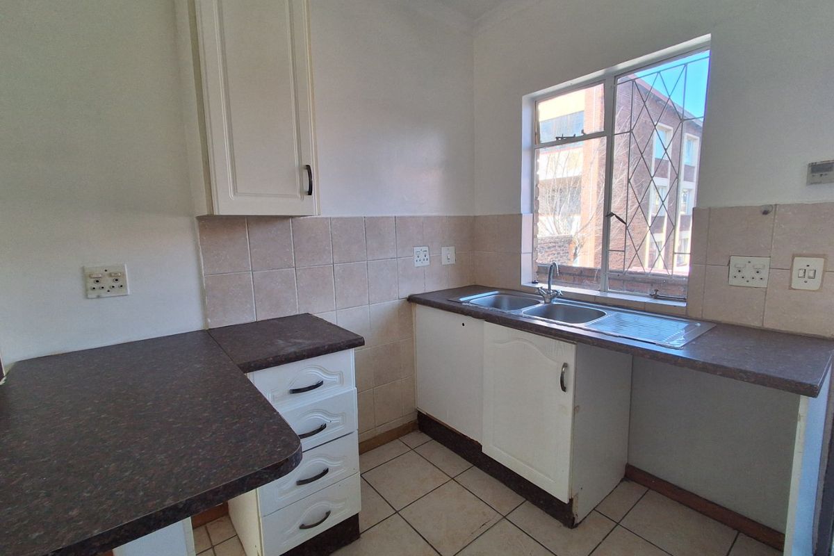 A functional kitchen featuring laminate countertops, a double bowl stainless steel sink, tiled splashback, and ample built-in cabinetry with ceramic floor tiles.