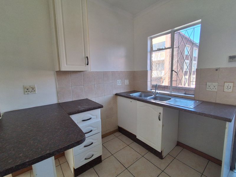 A functional kitchen featuring laminate countertops, a double bowl stainless steel sink, tiled splashback, and ample built-in cabinetry with ceramic floor tiles.