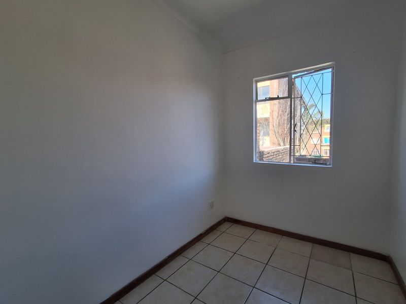 An empty bedroom featuring tiled flooring and a window fitted with security burglar bars.