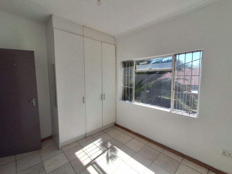 A vacant bedroom featuring built-in cupboards, tiled flooring, and a window fitted with security bars.