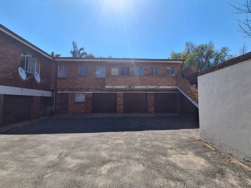 Exterior view of an apartment complex featuring a paved driveway, multiple garage units, and an external staircase leading to upper levels.