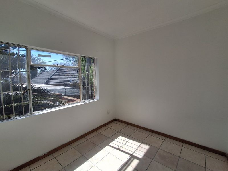 An empty bedroom featuring tiled flooring, neutral walls, and security bars on the window, providing a blank canvas for personalization.