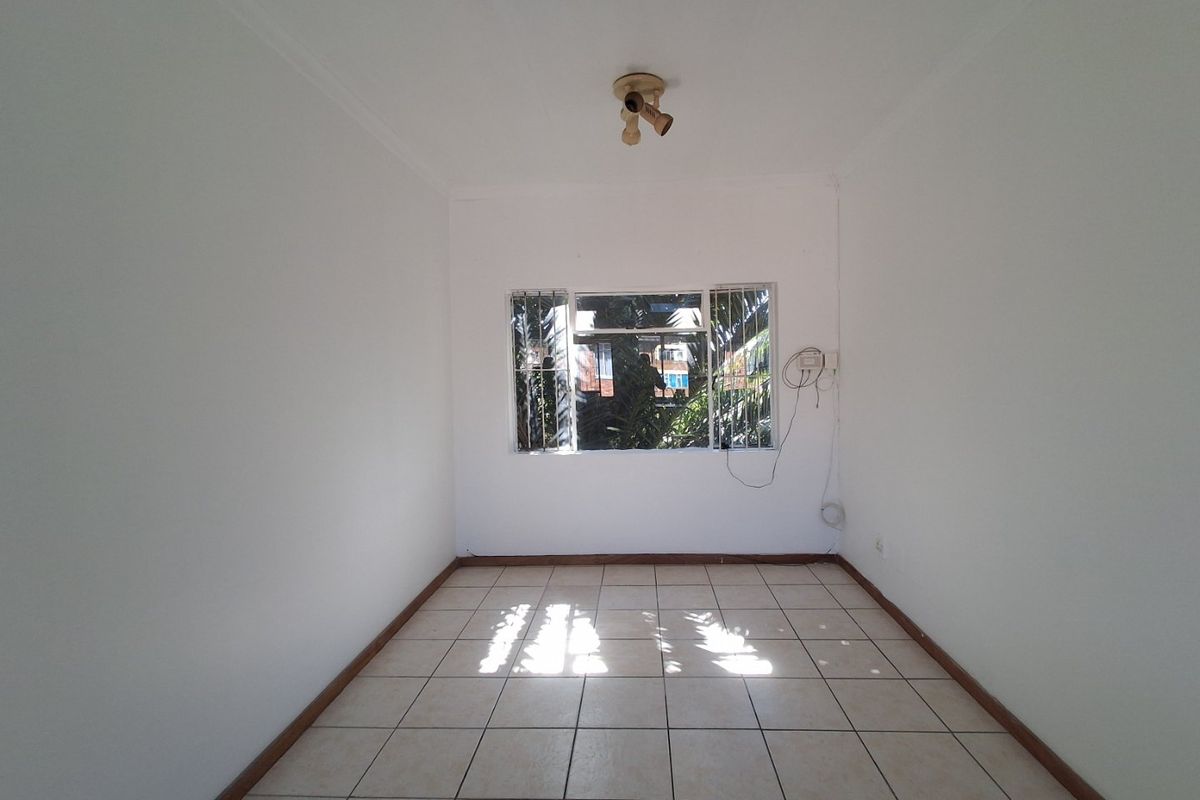 An empty bedroom featuring tiled flooring, a window with security bars, and a ceiling-mounted light fixture.