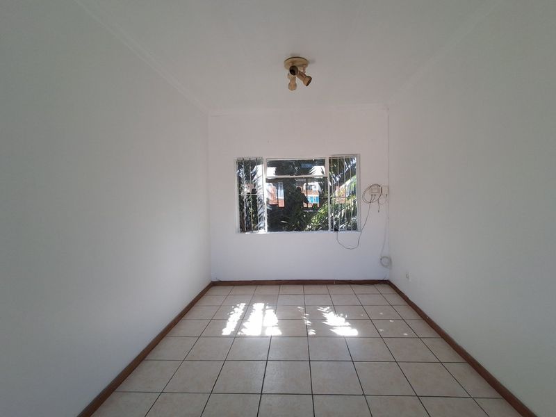 An empty bedroom featuring tiled flooring, a window with security bars, and a ceiling-mounted light fixture.