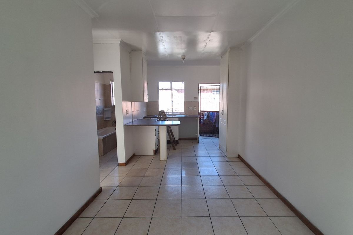 An empty open-plan living and kitchen area featuring tiled flooring, built-in cabinetry, and direct access to an exterior security gate.