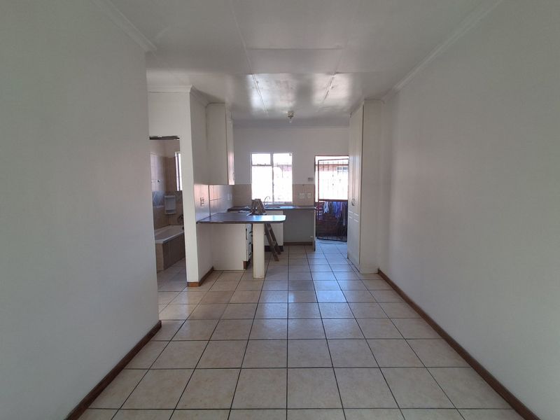 An empty open-plan living and kitchen area featuring tiled flooring, built-in cabinetry, and direct access to an exterior security gate.