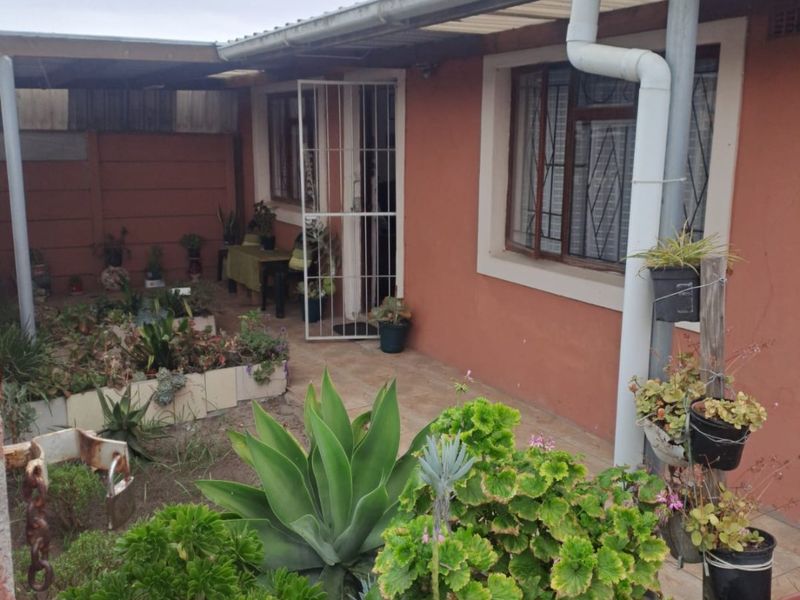 A covered patio area featuring tiled flooring, security gate, and direct access to the garden, providing a functional outdoor space for relaxation.