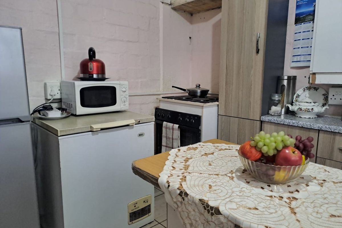 A compact kitchen area featuring built-in cabinetry, a freestanding stove, and tiled flooring, currently requiring cosmetic updates to the wall finishes and cabinetry.