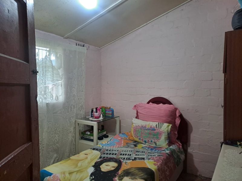 A compact bedroom featuring painted brick walls, an exposed beam ceiling, and a window fitted with security bars.
