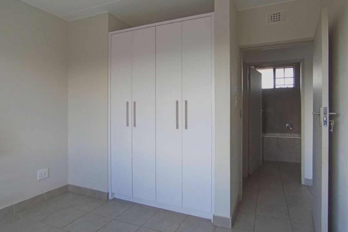 An empty bedroom featuring built-in wardrobes, tiled flooring, and direct access to an adjoining bathroom.