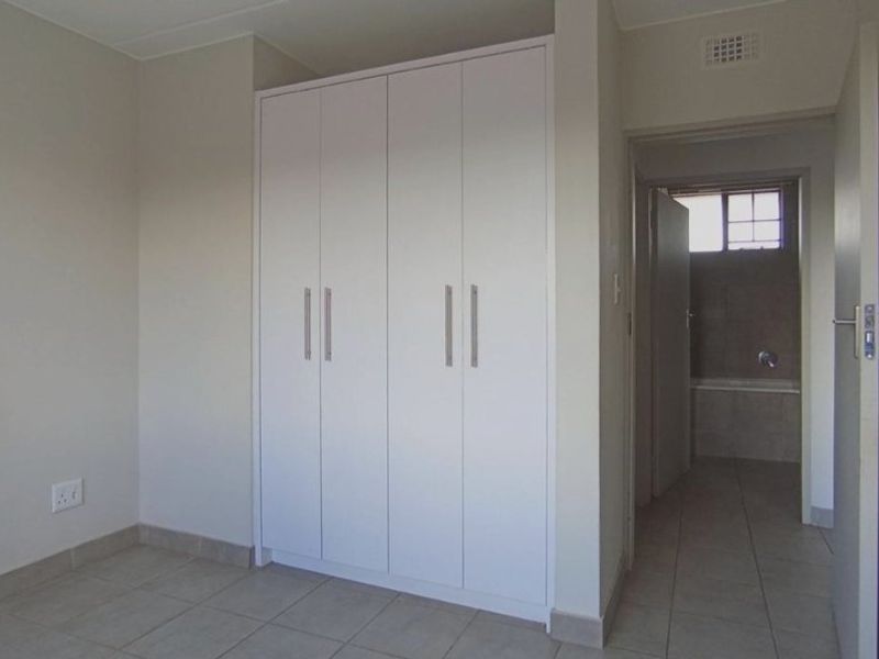 An empty bedroom featuring built-in wardrobes, tiled flooring, and direct access to an adjoining bathroom.