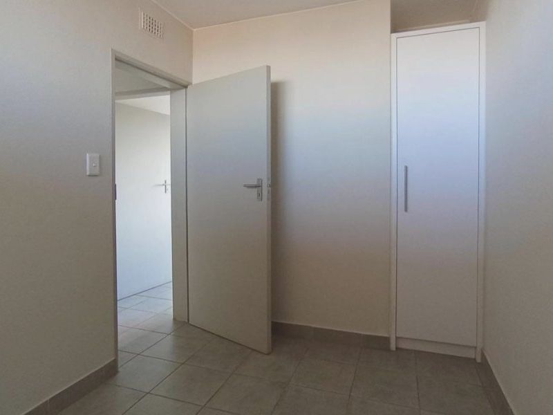 A clean, empty hallway featuring neutral tiled flooring and a built-in storage cupboard, providing a functional transition space within the apartment.