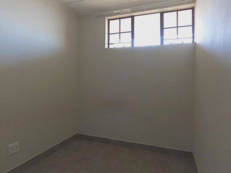 A compact, empty bedroom featuring tiled flooring and a high-level window, providing a neutral space ready for personalization.