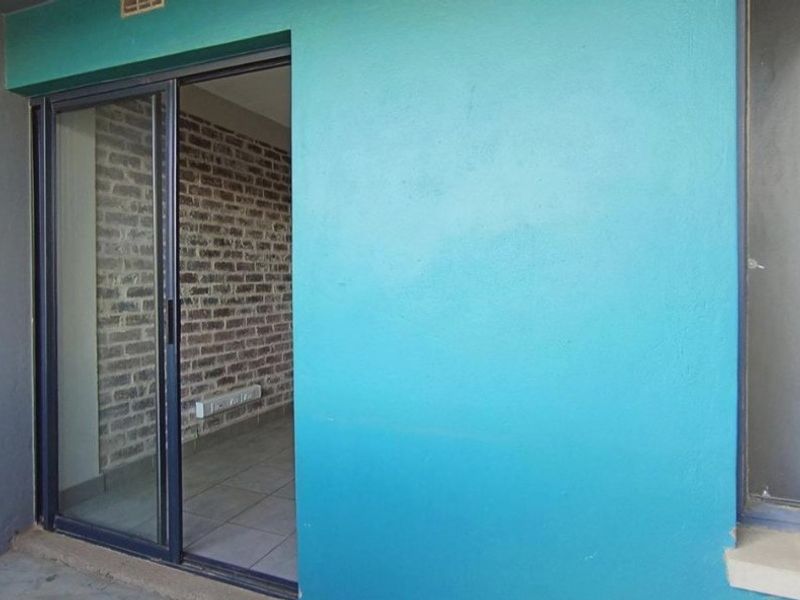 A covered balcony area featuring a sliding glass door entrance, exposed brick interior wall, and tiled flooring.