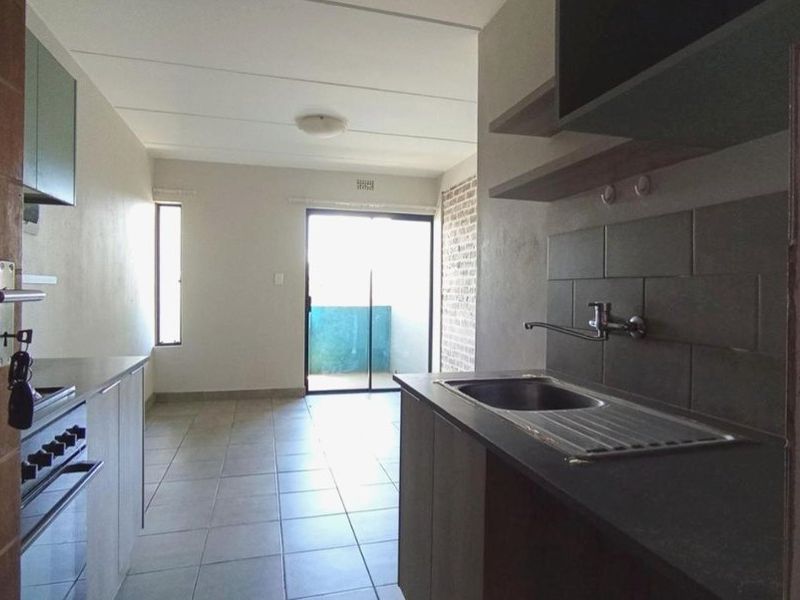 Open-plan kitchen and living area featuring tiled floors, built-in cabinetry, and a sliding door leading to a balcony.