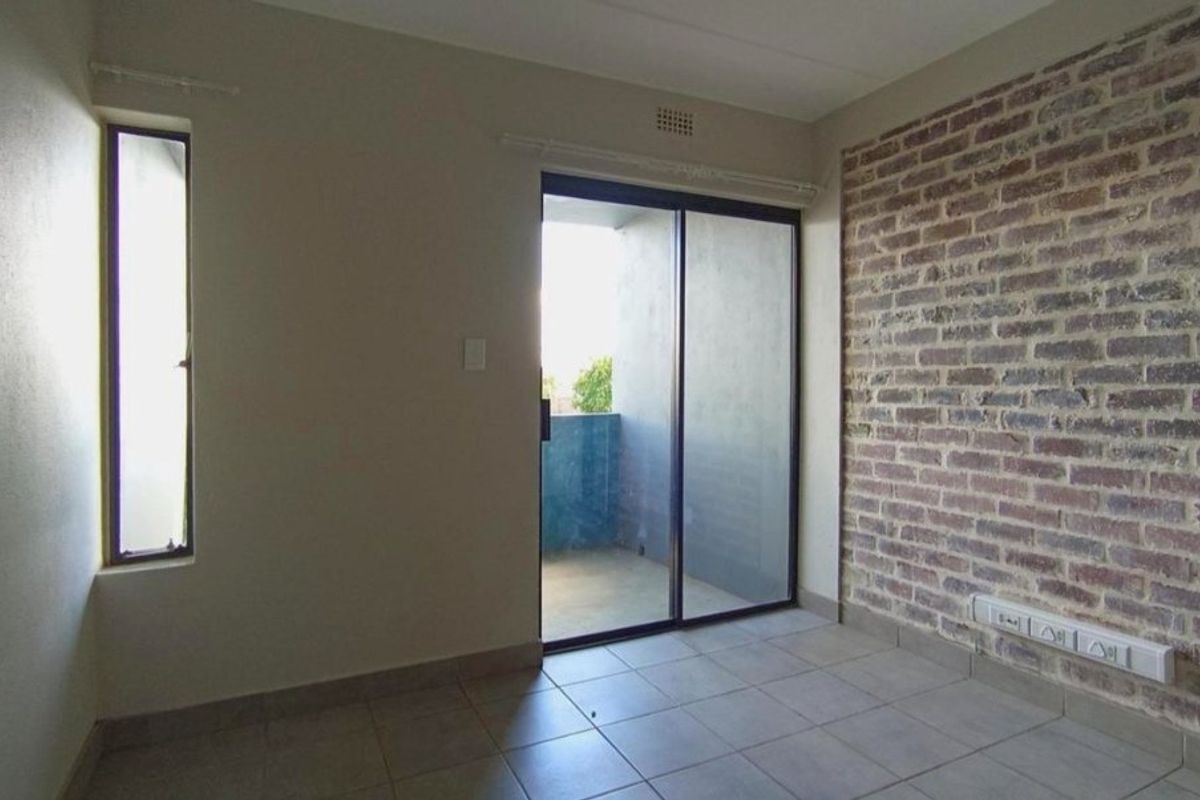 An empty living area featuring a rustic exposed brick wall, tiled flooring, and a sliding glass door providing access to a private balcony.