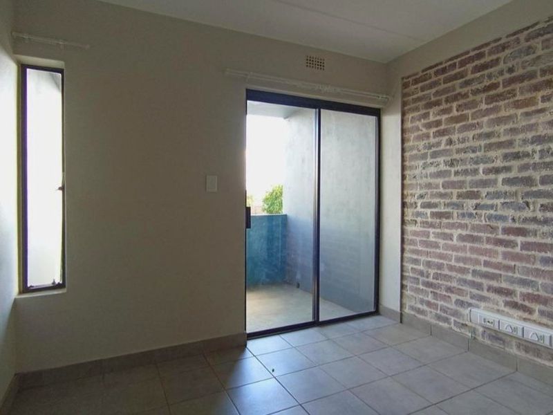 An empty living area featuring a rustic exposed brick wall, tiled flooring, and a sliding glass door providing access to a private balcony.