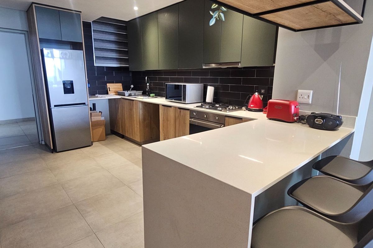Modern kitchen featuring sleek dark cabinetry, stone countertops, a breakfast bar, and integrated appliances with a stylish tiled backsplash.