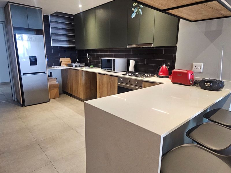 Modern kitchen featuring sleek dark cabinetry, stone countertops, a breakfast bar, and integrated appliances with a stylish tiled backsplash.
