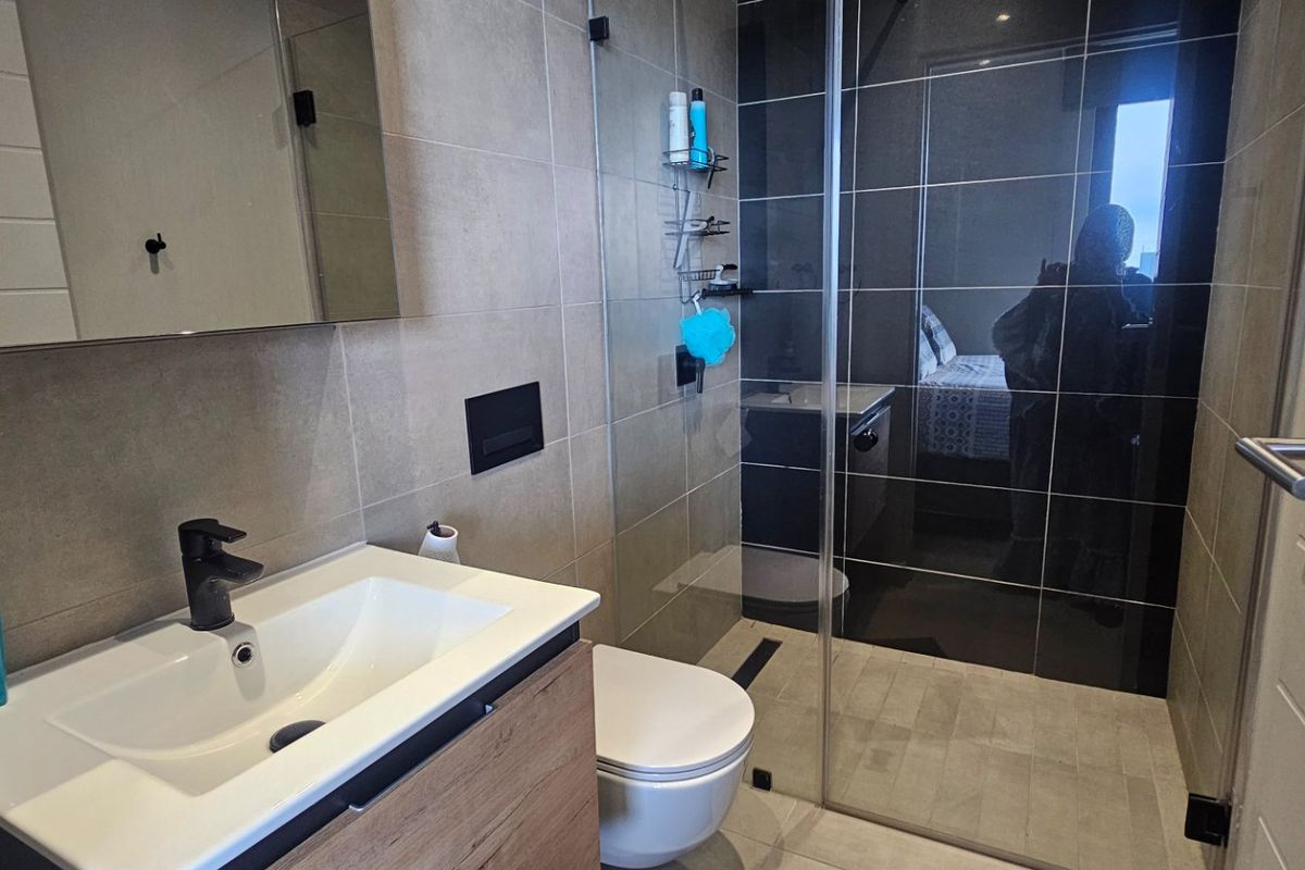 Modern bathroom featuring a vanity with basin, wall-mounted toilet, and a spacious walk-in shower with glass screen and contemporary black fixtures.