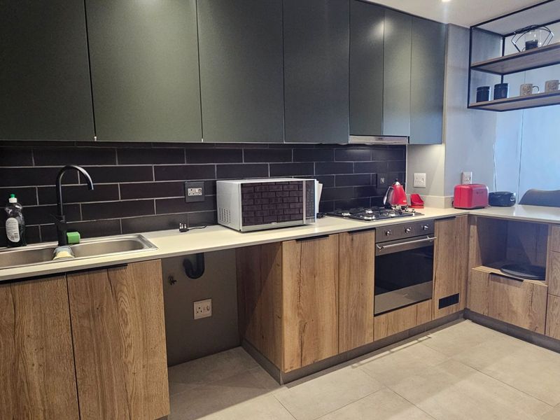 Modern kitchen featuring dark upper cabinetry, wood-grain lower cabinets, stone countertops, black subway tile backsplash, and integrated stainless steel appliances.