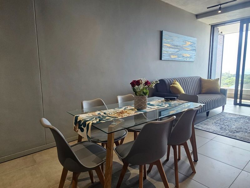 Modern open-plan living and dining area featuring large sliding glass doors leading to a balcony, neutral tiled flooring, and contemporary track lighting.