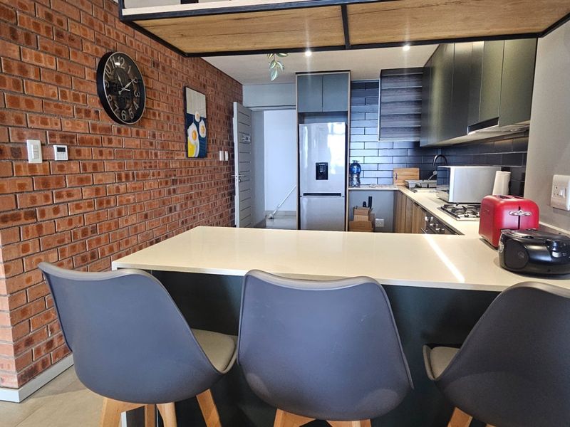 Modern kitchen featuring an exposed brick feature wall, sleek dark cabinetry, quartz countertops, and a breakfast bar with integrated appliances.