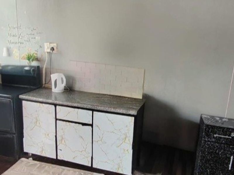 A compact kitchen area featuring built-in cabinetry, a stone-look countertop, tiled backsplash, and a freestanding stove, offering potential for modernization.