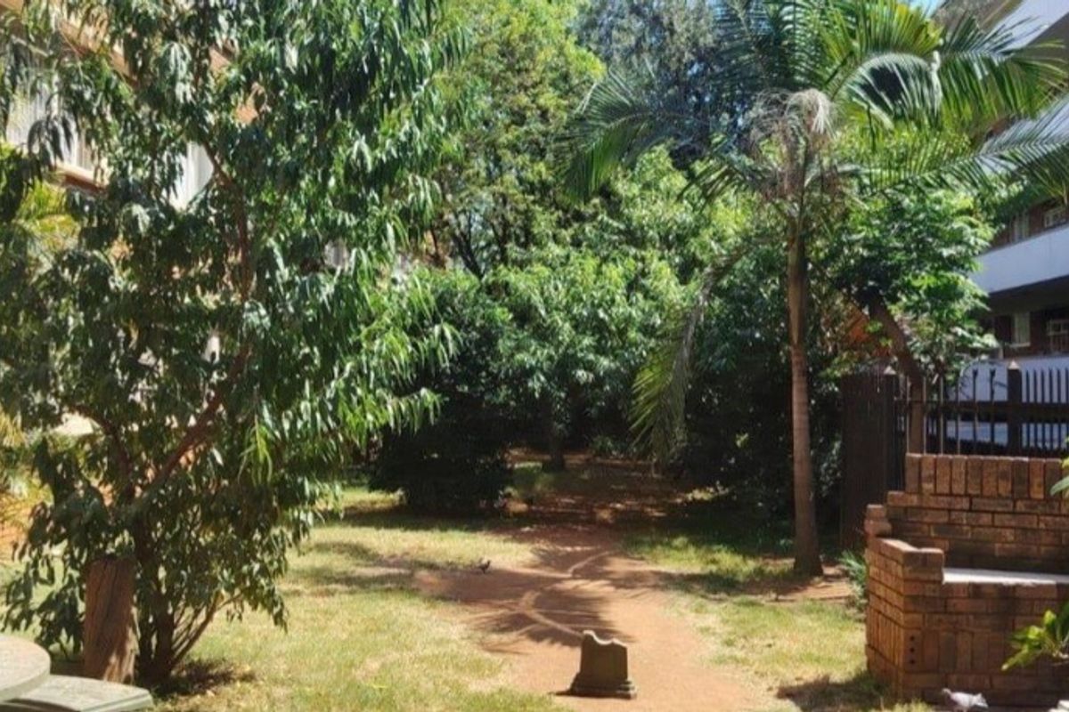 A communal garden area featuring mature trees, a palm tree, and a brick built-in seating structure.