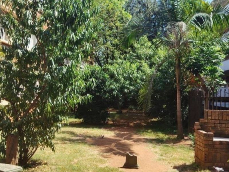 A communal garden area featuring mature trees, a palm tree, and a brick built-in seating structure.
