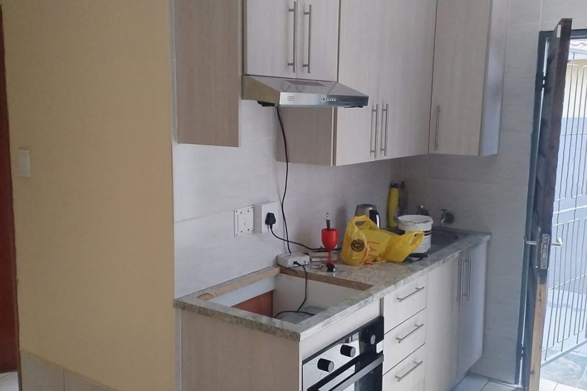 Compact kitchen featuring light wood-finish cabinetry, built-in oven, extractor fan, and tiled flooring, currently requiring completion of the cooktop and countertop installation.