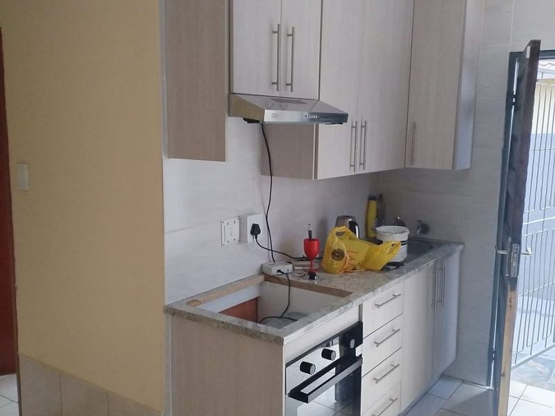 Compact kitchen featuring light wood-finish cabinetry, built-in oven, extractor fan, and tiled flooring, currently requiring completion of the cooktop and countertop installation.